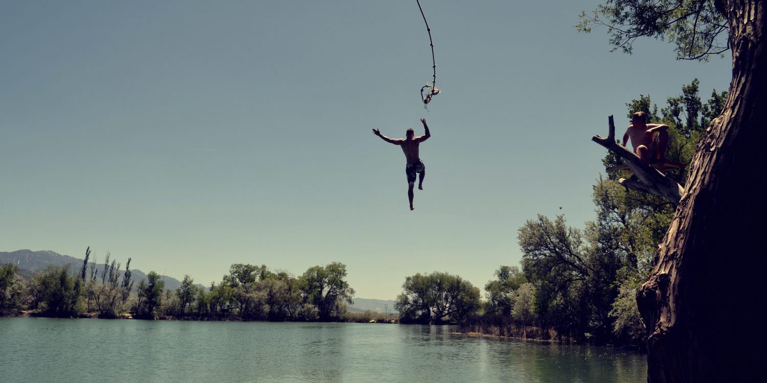 Mann, der an einer Liane hängt und in einen See springt