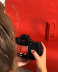 Eine Person fotografiert eine kleine rote Türe vor einem roten Hintergrund mit einer Spiegelreflexkamera.
