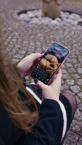 Frau sitzt auf einer Bank und schaut mit dem Handy Reels auf Instagram an 