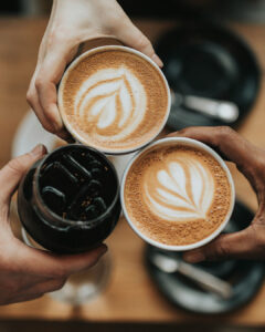 Drei Personen stoßen mit Kaffee und Eiskaffee an.